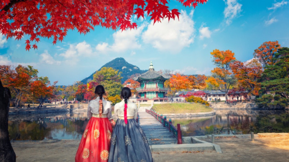 Two women in hanbok facing a pavilion and autumn scenery in South Korea