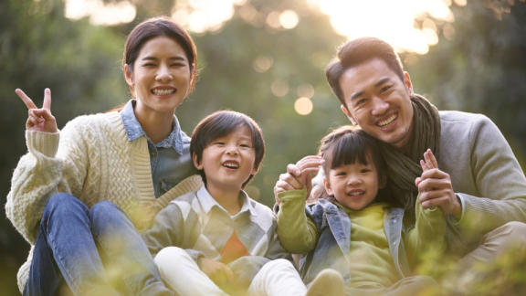 A Taiwanese family is sitting in a meadow and smiling at the camera
