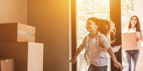 Happy family during private move – child runs joyfully into new home while parents carry moving boxes inside..