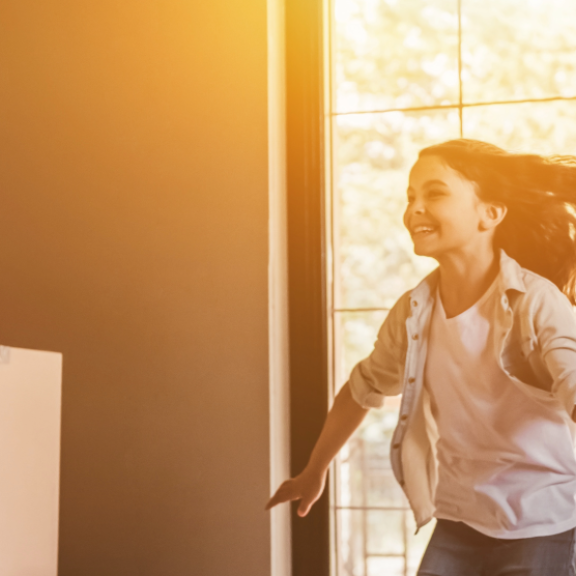 Happy family during private move – child runs joyfully into new home while parents carry moving boxes inside.