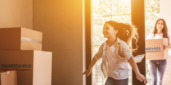 Happy family during private move – child runs joyfully into new home while parents carry moving boxes inside..