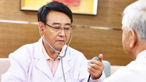 A doctor from Singapore is taking an elderly patient's vital signs with a stethoscope