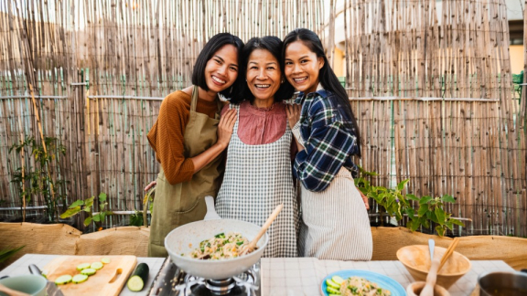 A Filipino mother is cooking with her adult daughters and posing for a photo with them.
