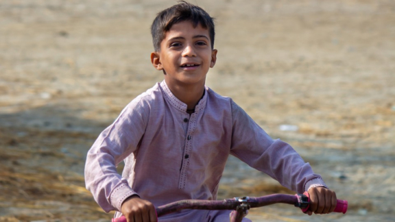 A boy from Pakistan is riding his bike down a country road