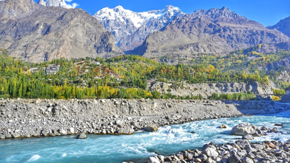 A rocky landscape in Pakistan featuring a river, scattered forests, and a mountain range