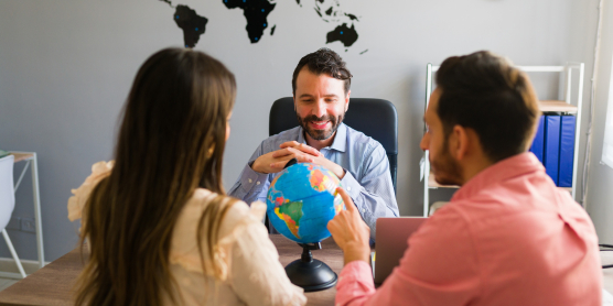 Beratungsgespräch zwischen Relocation Service für Expats und Paar in modernem Büro mit Weltkarte im Hintergrund.
