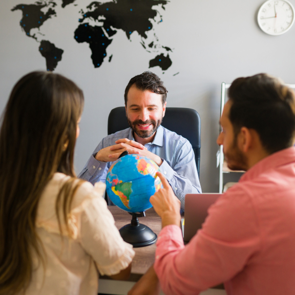 Consultation between relocation service for expats and couple in modern office with world map in the background.