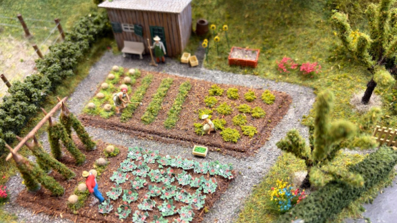Detaillierte Modelleisenbahnanlage mit Miniatur-Figuren im Garten, deren lose Kleinteile vor dem Transport mit DACHSER & KOLB abgenommen werden müssen.