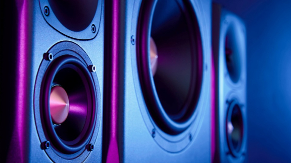 Mehrere hochwertige HiFi-Lautsprecher mit empfindlichen Membranen im violetten Neonlicht vor dem sicheren Umzugstransport durch DACHSER & KOLB.