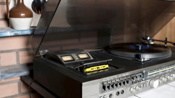Ein klassischer HiFi-Plattenspieler mit geöffneter Staubschutzhaube und Tonarm auf einer Musikanlage vor dem sicheren Umzug mit DACHSER & KOLB.