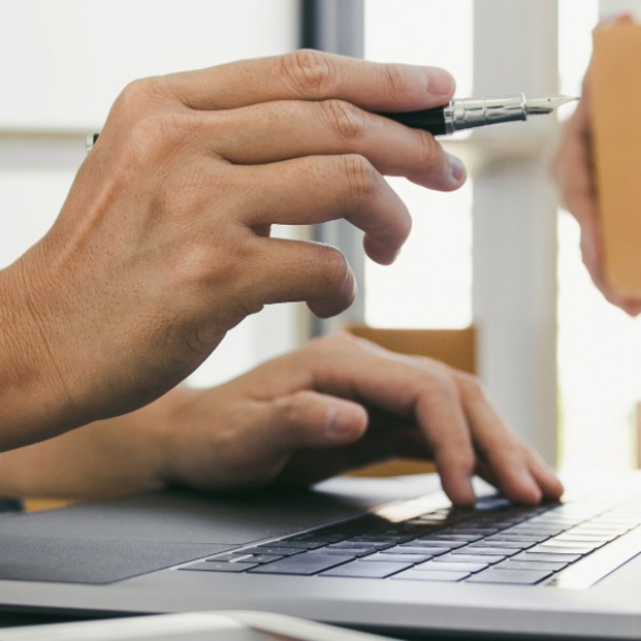 A coordinator working on a laptop next to a moving box and packing tape – symbol image for the strategic procurement of moving and relocation services in B2B procurement.
