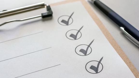 A structured checklist with completed tick boxes on a clipboard beside a pen – symbol image for transparent project execution by DACHSER & KOLB.