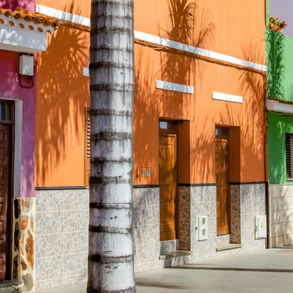 Bunte Häuserfassaden in Pink und Orange an einer mit Palmen gesäumten Straße auf Teneriffa, genutzt als Symbolbild für den Versand von Umzugskartons mit DACHSER & KOLB.