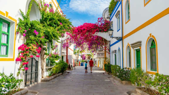 Eine idyllische Gasse mit weißen Häusern und blühenden Bougainvillea in Puerto de Mogán auf Gran Canaria, ideal für den Transport von Umzugskartons mit DACHSER & KOLB.