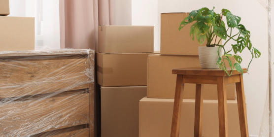 A wooden dresser wrapped in protective stretch film next to stacked moving boxes in a bright apartment, ready for small volume transport with DACHSER & KOLB.