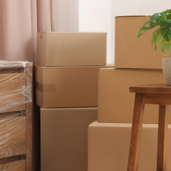 A wooden dresser wrapped in protective stretch film next to stacked moving boxes in a bright apartment, ready for small volume transport with DACHSER & KOLB.