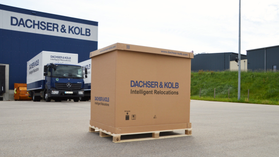 A large DACHSER & KOLB pallet box on a wooden pallet in front of company trucks, used for the secure transport of small volumes.