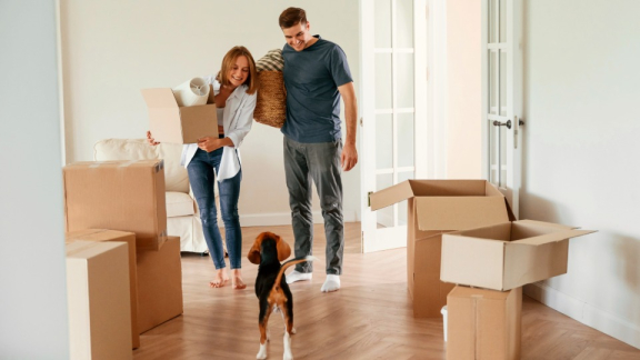 A happy couple carrying packed moving boxes in a bright apartment, preparing for small volume transport with DACHSER & KOLB.