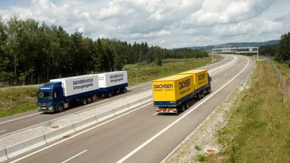 A DACHSER & KOLB moving logistics truck and a DACHSER intelligent logistics truck driving side by side on a road during transport in Europe.