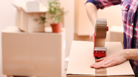Close-up of a person sealing a moving box with tape. Symbolizing relocation service for expats.