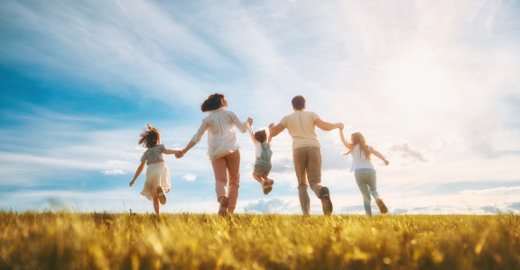 Family happily running on a meadow – Symbol image for Relocation Service for Expats.