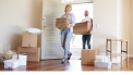 Couple carrying moving boxes and baskets into new home – tips and support in the moving guide