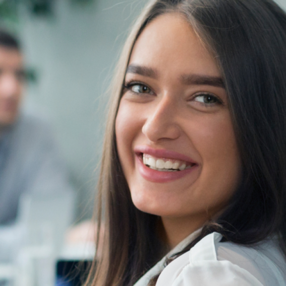 Eine lächelnde junge Frau im Vordergrund einer Gruppe während einer Ausbildungsveranstaltung.