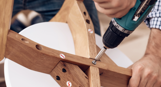 Möbelmontage leicht gemacht: Person schraubt Holzstuhl zusammen mit Akkuschrauber, Schritt-für-Schritt-Anleitung sichtbar