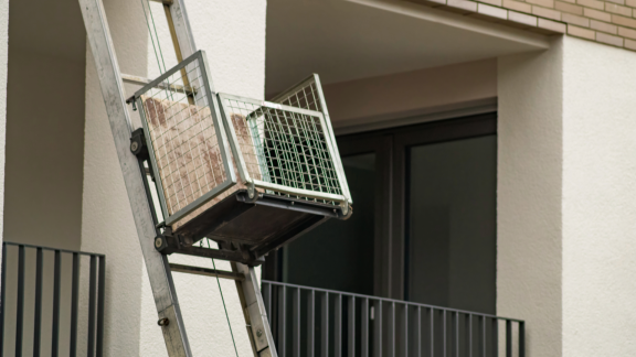 Außenaufzug mit Gitterplattform transportiert Karton zum Balkon eines Wohnhauses.