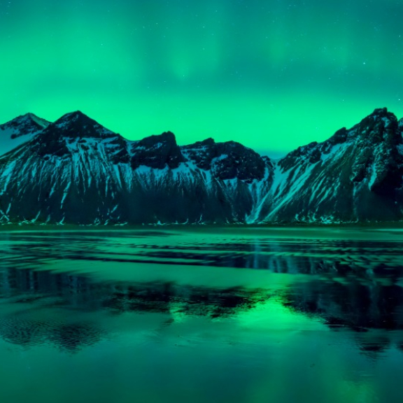Northern lights over snow-covered mountains and reflective water in Iceland