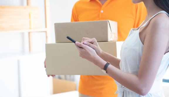 Frau bestätigt Proof of Delivery (POD) auf Smartphone, während Zusteller Pakete übergibt.