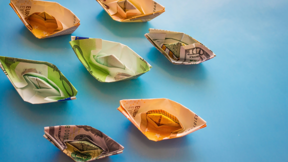 Gefaltete Papierboote aus Euro- und Dollar-Scheinen auf blauem Hintergrund