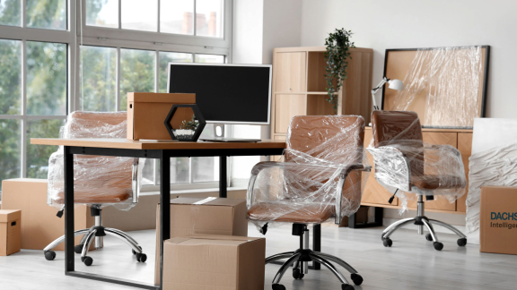 Büroraum mit verpackten Drehstühlen, Schreibtisch und Kartons, Emballage für Büroumzug