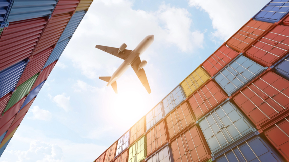 Flugzeug über gestapelten bunten Containern – Symbol für Terminal Handling Charges im globalen Handel.