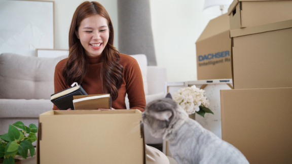 Frau packt Umzugskarton mit Katze – Ihr Tierumzug in die Schweiz mit DACHSER & KOLB.