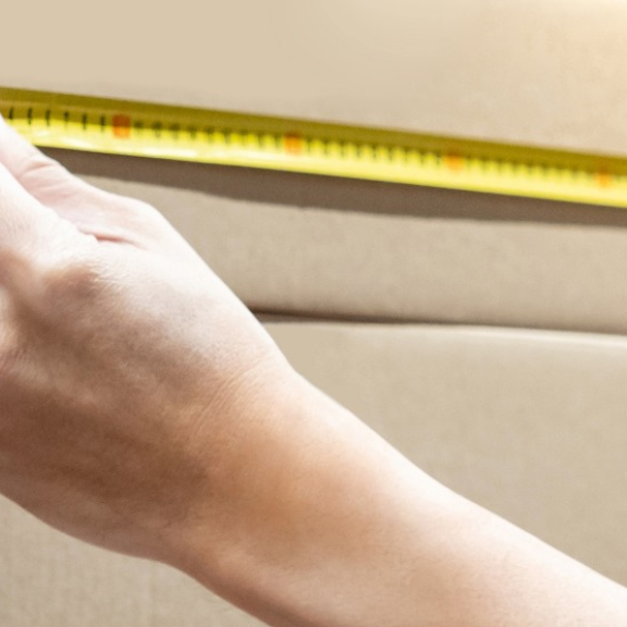 Person misst Höhe eines Kartons mit Maßband zur Berechnung des Volumens