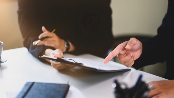 Zwei Personen prüfen Unterlagen zur Ladungssicherung an einem Schreibtisch.