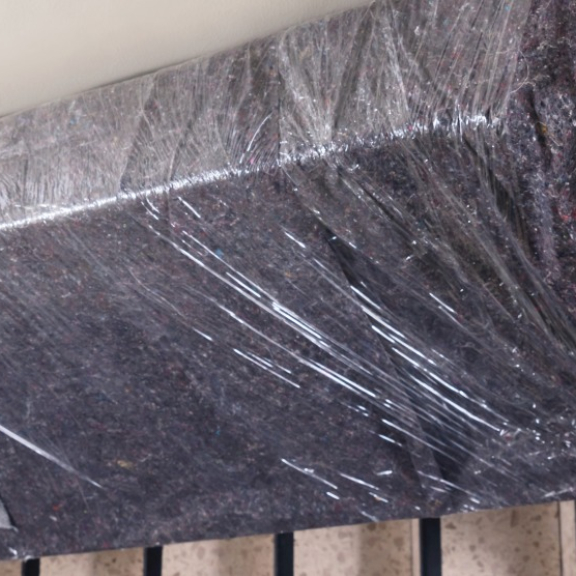 Zwei Umzugshelfer tragen ein mit Decke und Folie geschütztes Sofa vorsichtig durch das Treppenhaus.