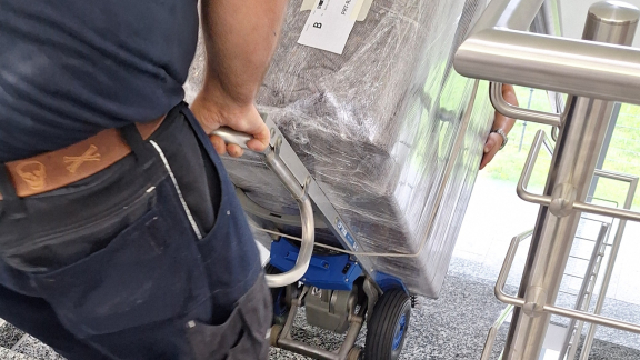 Mitarbeiter transportiert verpacktes Möbelstück mit einem Treppensteiger sicher eine Treppe hinauf.