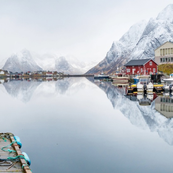 Fjorddorf in Norwegen mit schneebedeckten Bergen und Spiegelung im ruhigen Wasser