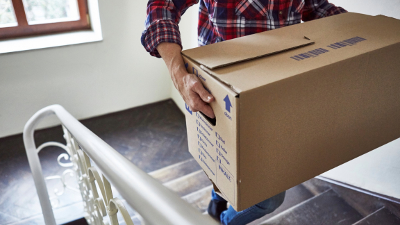 Träger transportiert Umzugskarton im Treppenhaus – Unterstützung beim Einzug am Zielort