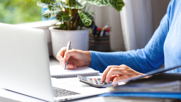 Person plant den Einzug am Zielort am Laptop und berechnet Kosten mit Taschenrechner