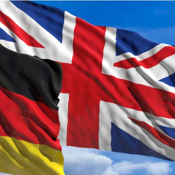 Deutsche und britische Flagge wehen nebeneinander vor blauem Himmel als Symbol für Zoll UK nach Deutschland.