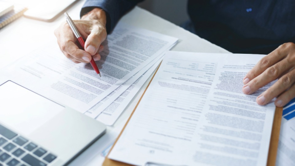 Person prüft Zollunterlagen am Schreibtisch mit Stift, Formularen und Laptop als Symbol für Zoll UK nach Deutschland