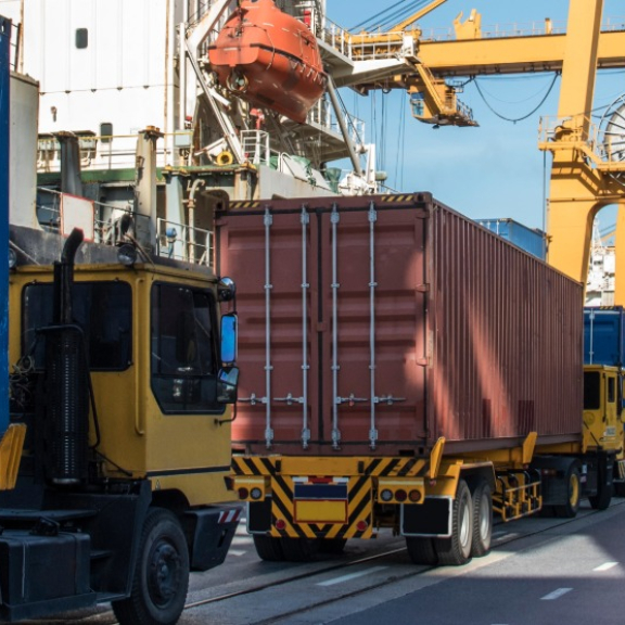 LKW mit Containern im Containerterminal, Hafenkräne im Hintergrund – TEU-basierte Containerlogistik