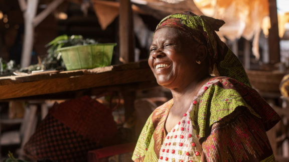 Portrait einer Frau in buntem Gewand vor einer einfachen Hütte