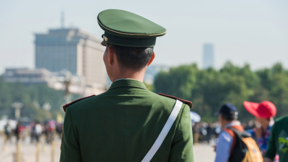 Uniformierter Wachposten in grüner Militäruniform mit Blick auf eine Menschenmenge in einer chinesischen Großstadt – Sicherheit bei der Auswanderung nach China